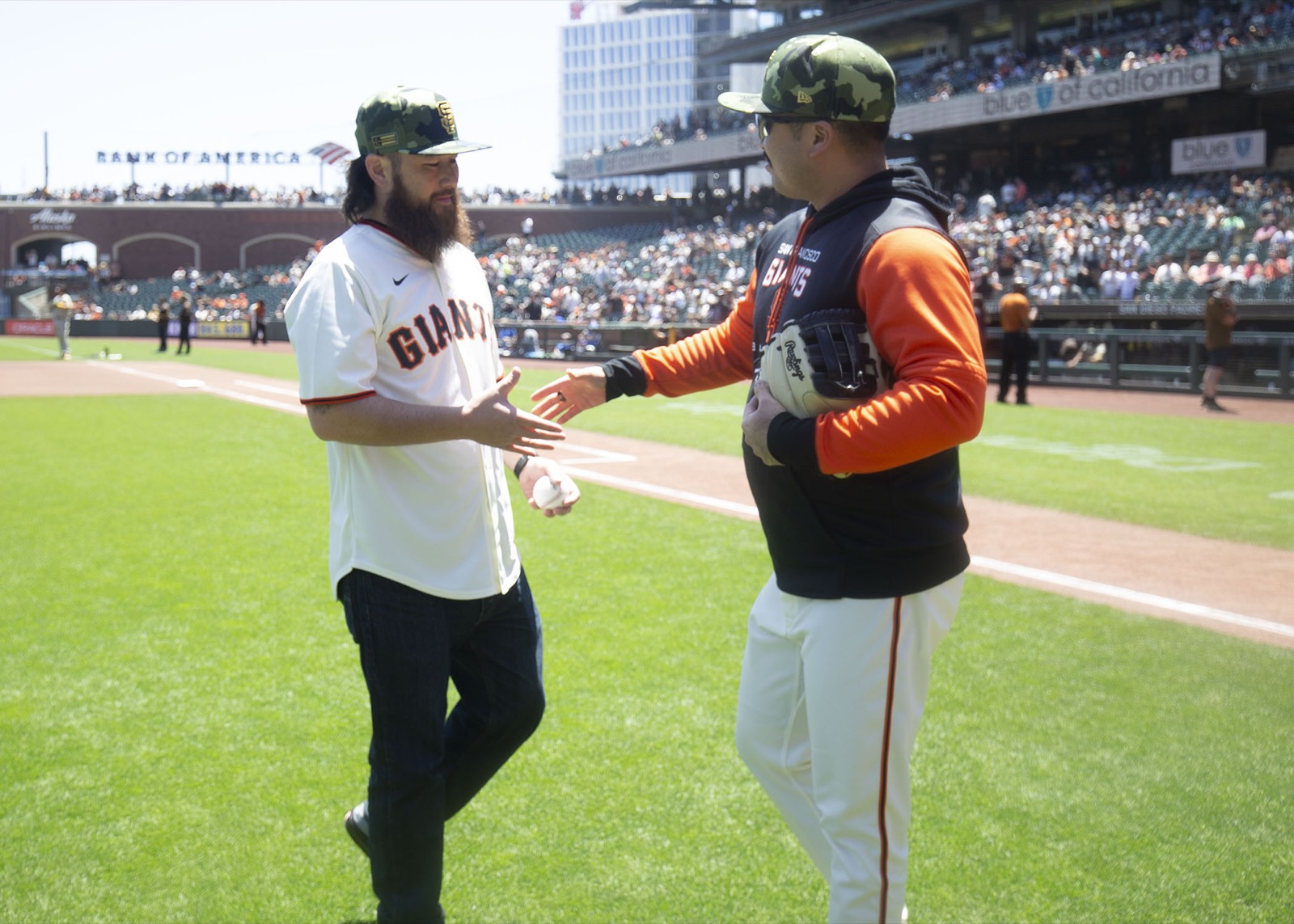 A veteran in a Giants jersey and a Giants player reaching to shake hands on the field before a game.