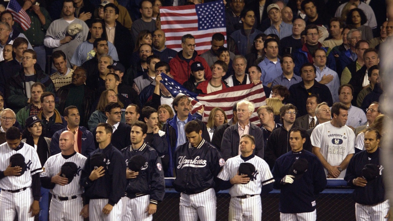 New York Yankees players and fans standing for the national anthem, American flags held up throughout the stands.